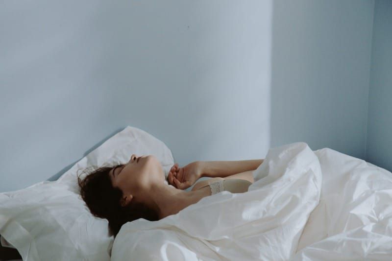 A woman lying awake in bed with white sheets, representing the nervous system hyperarousal and sleep difficulties common in highly sensitive people
