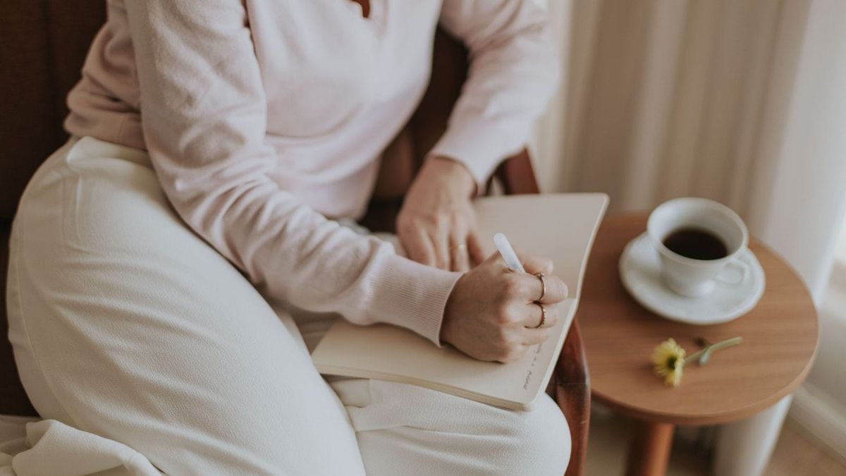 A person writing in a journal beside a softly lit window and a cup of tea, representing a moment of emotional grounding.