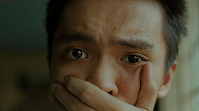 Close-up of a person covering their mouth with one hand.