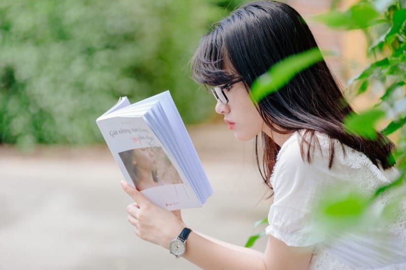 一位女性側身拿著一本打開的書閱讀。