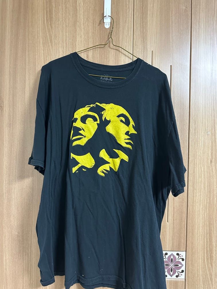 검은 배경 티셔츠에, 노란 구체의 표면을 사람의 얼굴들이 덮고 있는 모습이 단순한 그림자로 표현되어 있는 도안이 배치되어 있다.