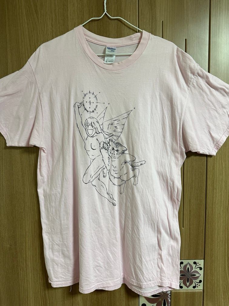 연분홍색 티셔츠에 긴 머리 여성 천사와 살찐 고양이가 날고 있는 도안이 그려져 있다.