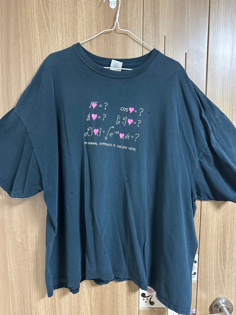 검은 티셔츠의 가슴에, 핑크색 하트를 주인공으로 하는 여러 수식의 계산 결과로 물음표가 제시되어 있고, "My normal approach is useless here."라는 문장이 적혀 있다.