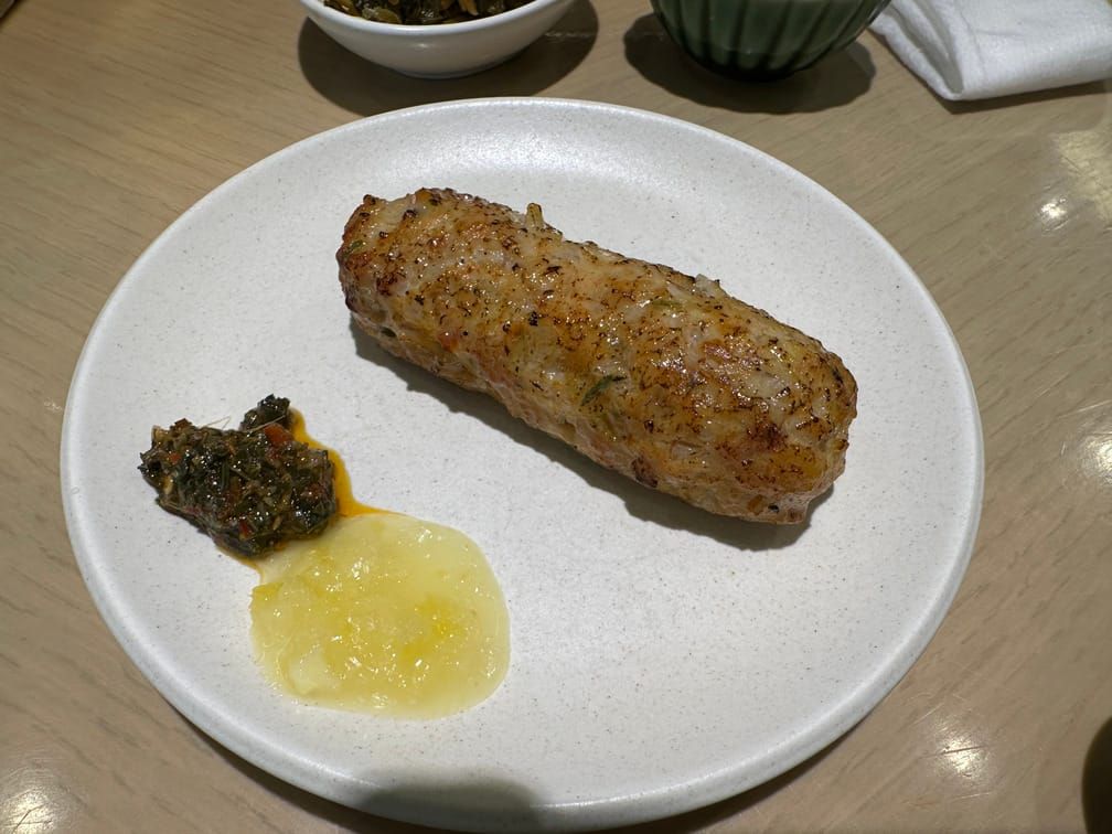 그릇에 기둥 모양으로 빚어진 연갈색으로 구워진 고기가 노란 소스와 풀이 붉은 국물에 절여진 소스와 함께 차려져 있다.