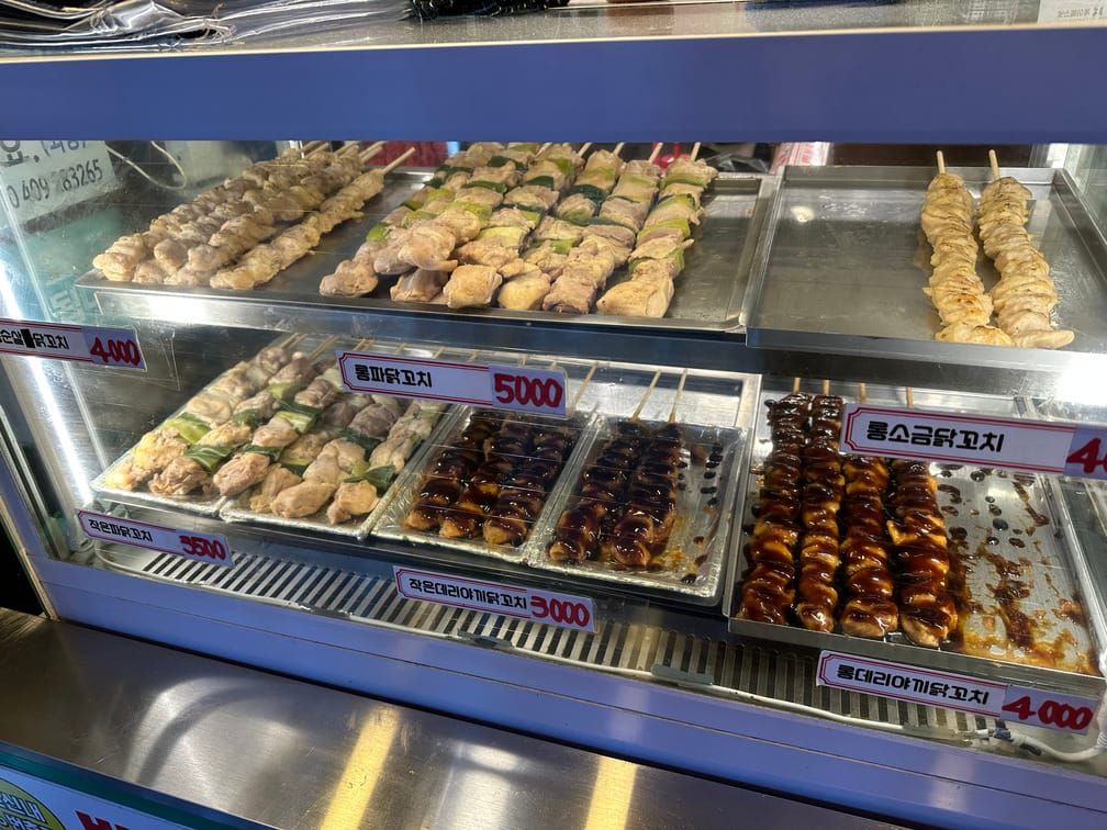 가게의 히터에 소스가 뿌려져 있거나 뿌려져 있지 않은 닭꼬치들이 다양하게 분류되어 진열되어 있고 가격표가 붙어 있다.