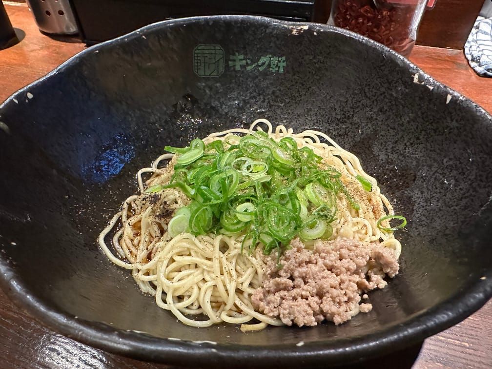 검은 면기에 가는 면이 담겨 있고 후추, 다진 고기, 채썬 대파가 올라가 있다.