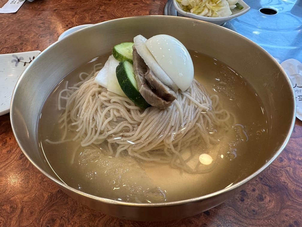면기에 차려진 맑은 국물 냉면. 고명으로 달걀, 배, 고기, 오이, 절인 무가 올라와 있다.