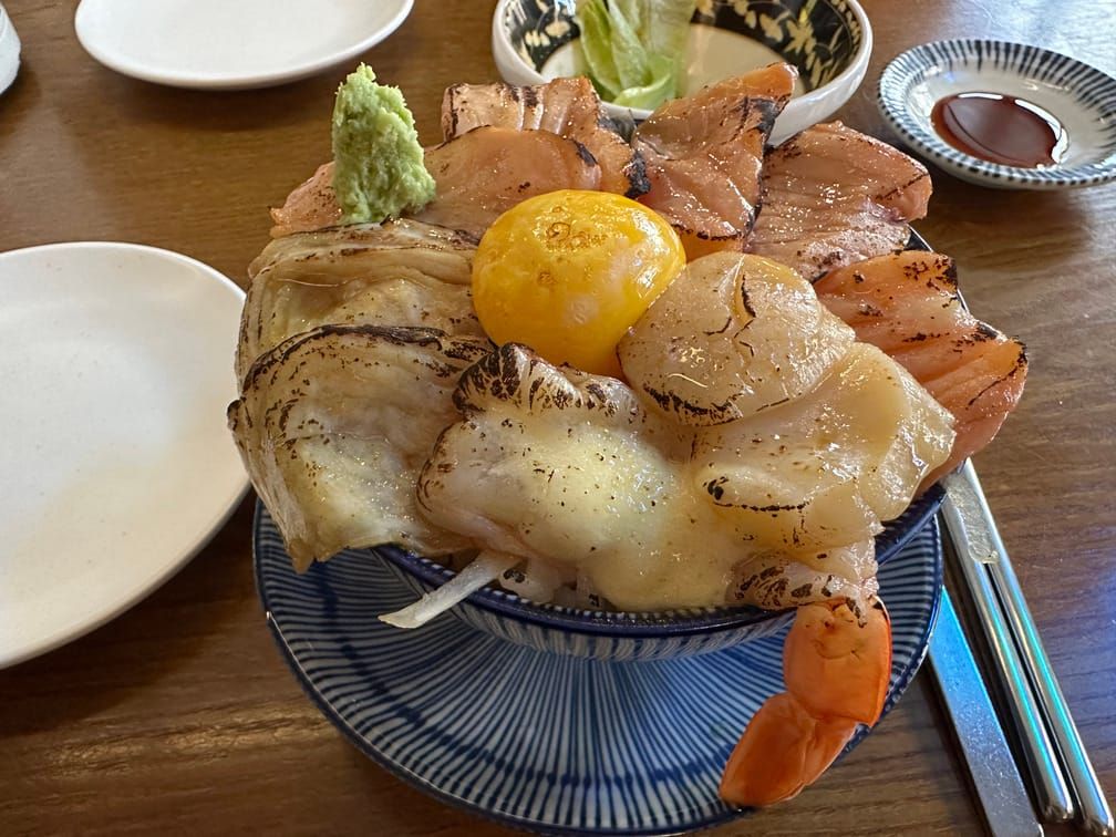 덮밥 그릇에 아부리한 새우, 관자, 연어와 달걀 노른자가 올라가 있고 와사비가 한움큼 올라가 있다.