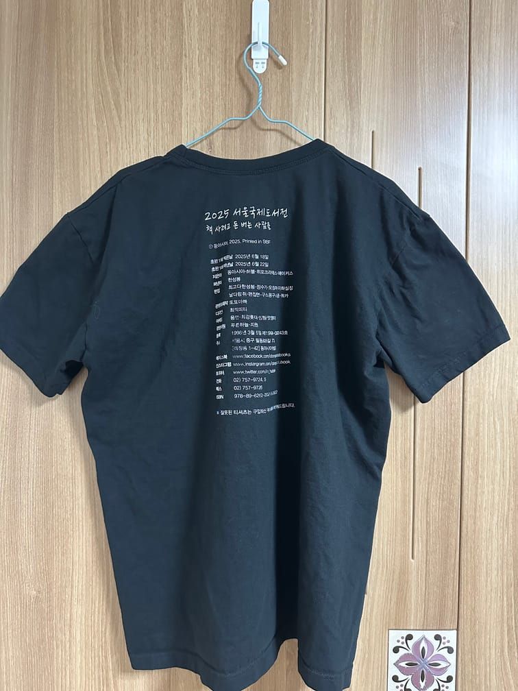 검은 티셔츠에 흰 글씨로 책의 판권지같은 내용이 인쇄되어 있다. 책(?)의 제목은 "2025 서울국제도서전", 부제는 "책 사려고 돈 버는 사람들"이다.