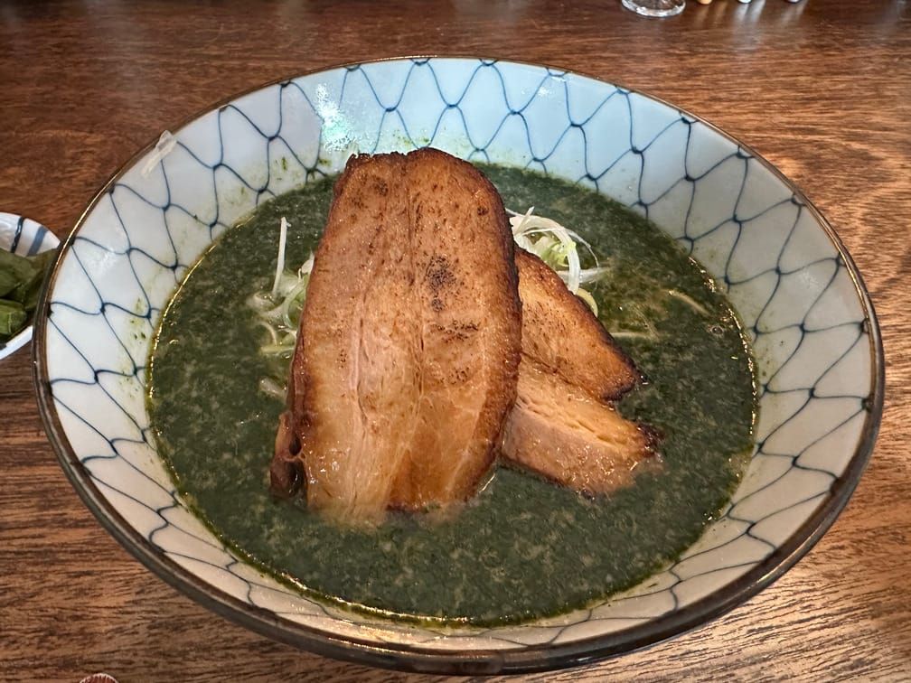 면기 안에 녹색 국물이 담겨 있고 채썬 양파, 챠슈가 떠 있다.