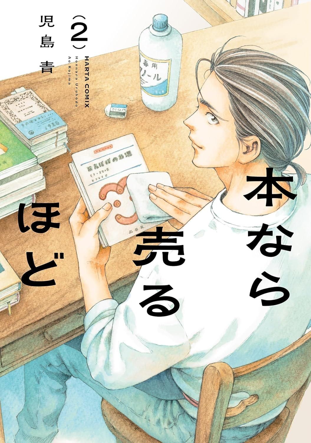 일본어 만화 『本なら売るほど』 2권의 표지. 책상에 앉아 책의 표지를 수건으로 닦는 머리를 묶은 남성을 어깨 뒤에서 내려다보는 구도의 일러스트.