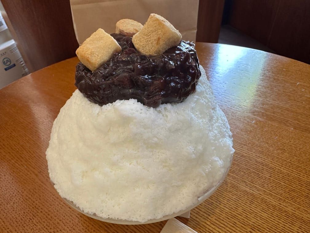 나무 테이블에 올라와 있는 빙수 그릇. 흰 우유얼음, 단팥, 인절미가 차례로 쌓여 있다.