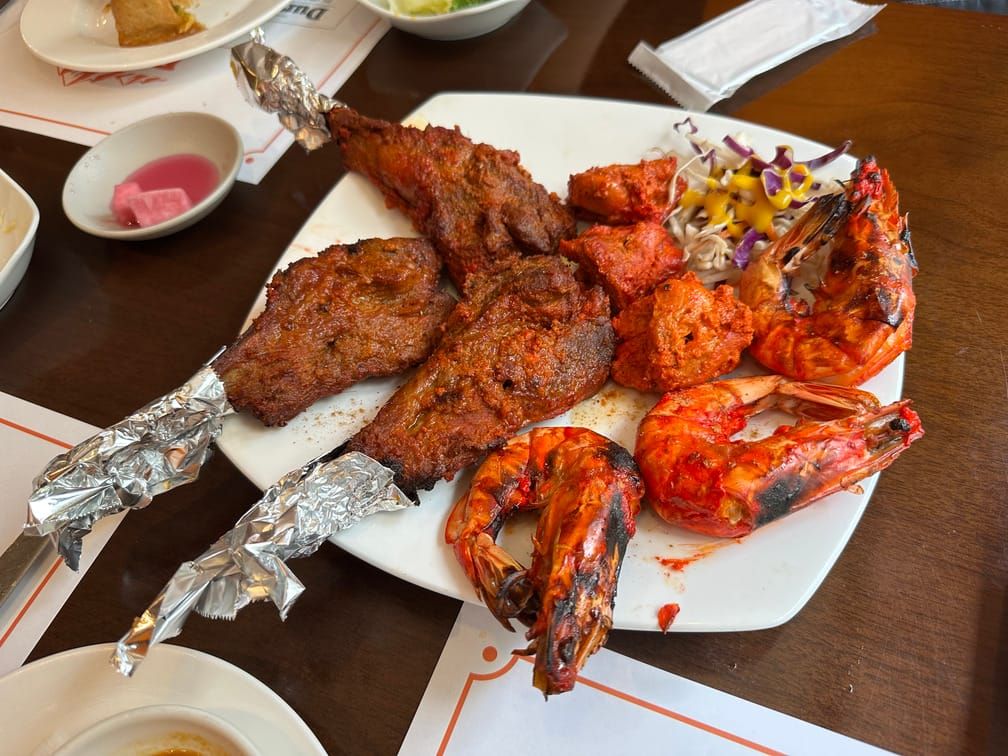 식탁 위의 접시에 탄두리 식으로 조리된 양다리, 새우, 닭고기와 약간의 샐러드가 올라가 있다.