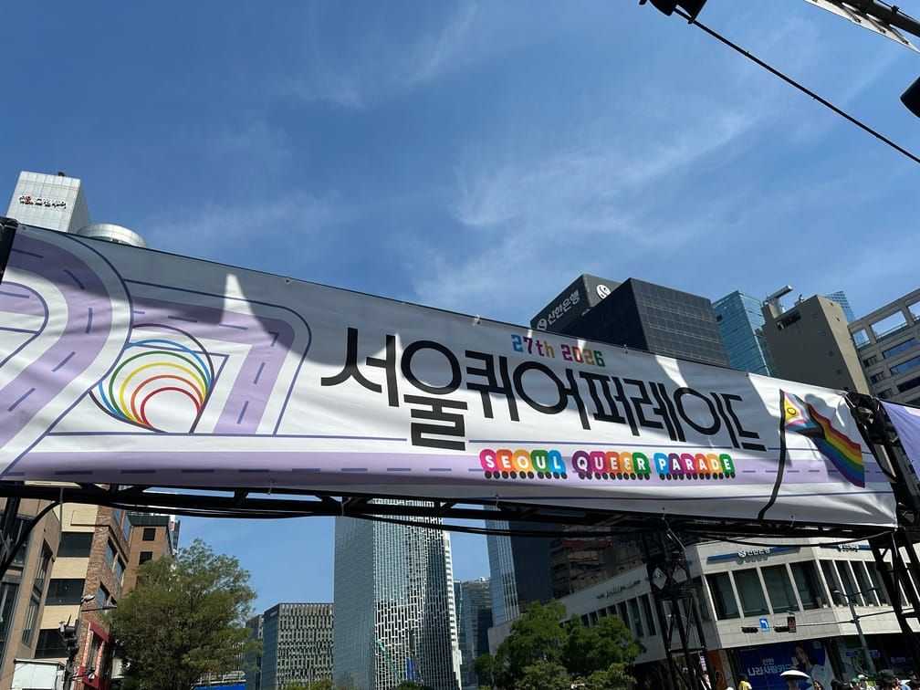 서울퀴어퍼레이드라는 제목의 현수막이 걸려 있는 야외의 가설 게이트의 사진.