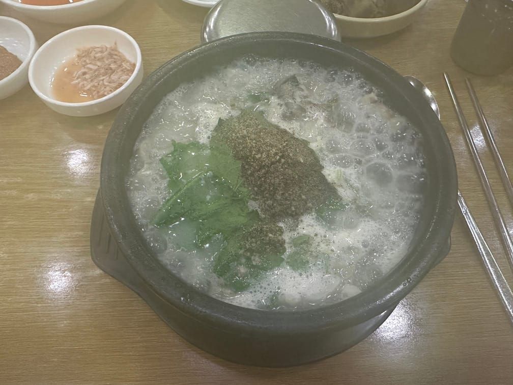 김이 뿌옇게 낀 사진. 뚝배기 안의 팔팔 끓는 흰 국물, 깻잎, 들깻가루 잔뜩. 새우젓 종지도 보인다.