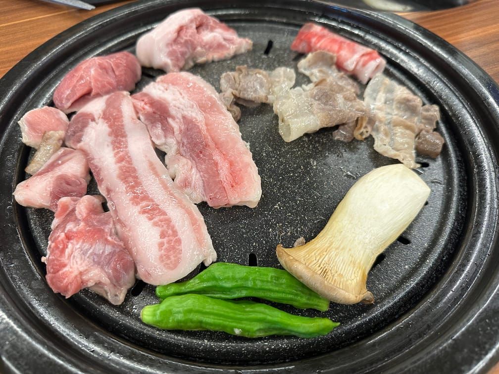 돌판 위에 올라와있는 삼겹살, 목살, 꽈리고추, 새송이버섯, 대패삼겹 등.
