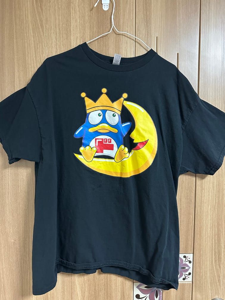 검은 티셔츠의 가슴 부분에 펭귄이 웃는 초승달 위에 앉아있는 모습이 그려져 있다. 펭귄의 배에는 일본어 가타가나 ド(도)가 적혀 있다.