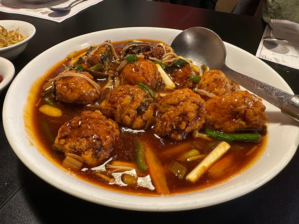 접시에 붉고 기름진 국물에 담긴 튀김 요리가 차려져 있다.