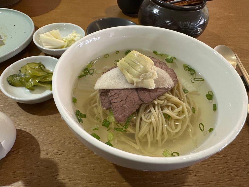 흰 그릇에 차려져 있는 파스타면 정도 굵기의 면이 맑은 국물 안에 있고, 소고기, 썬 무 등의 토핑이 올라가 있다.