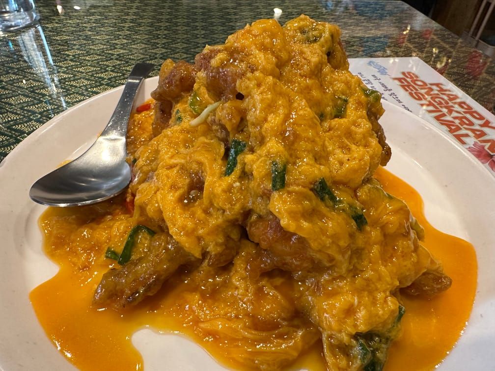 그릇에 노란 커리와 계란물, 녹색 야채로 덮인 젖은 튀김 음식이 차려져 있다.