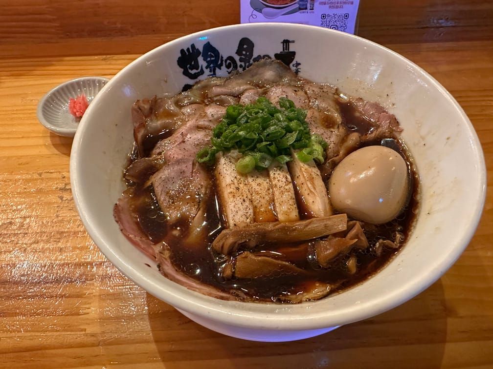 그릇에 검은 국물의 라멘이 차려져 있는 모습. 얇은 차슈, 두꺼운 고기, 간장 먹은 달걀, 원형썰기된 파.