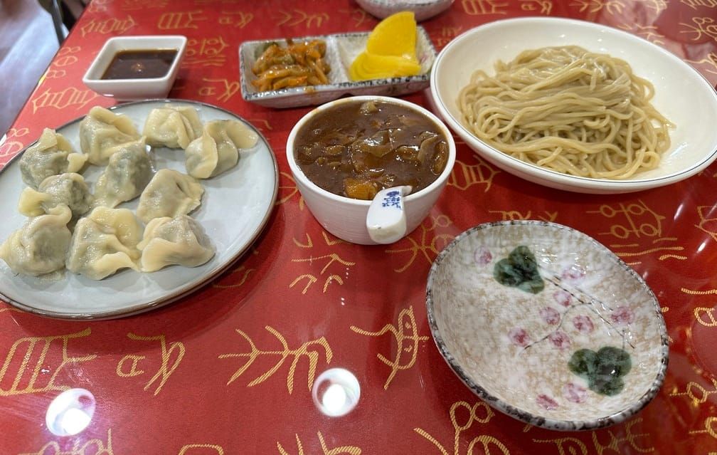 한자 상형문자 테이블보 위에 면, 갈색 짜장, 만두 접시와 단무지 등이 차려진 접시.