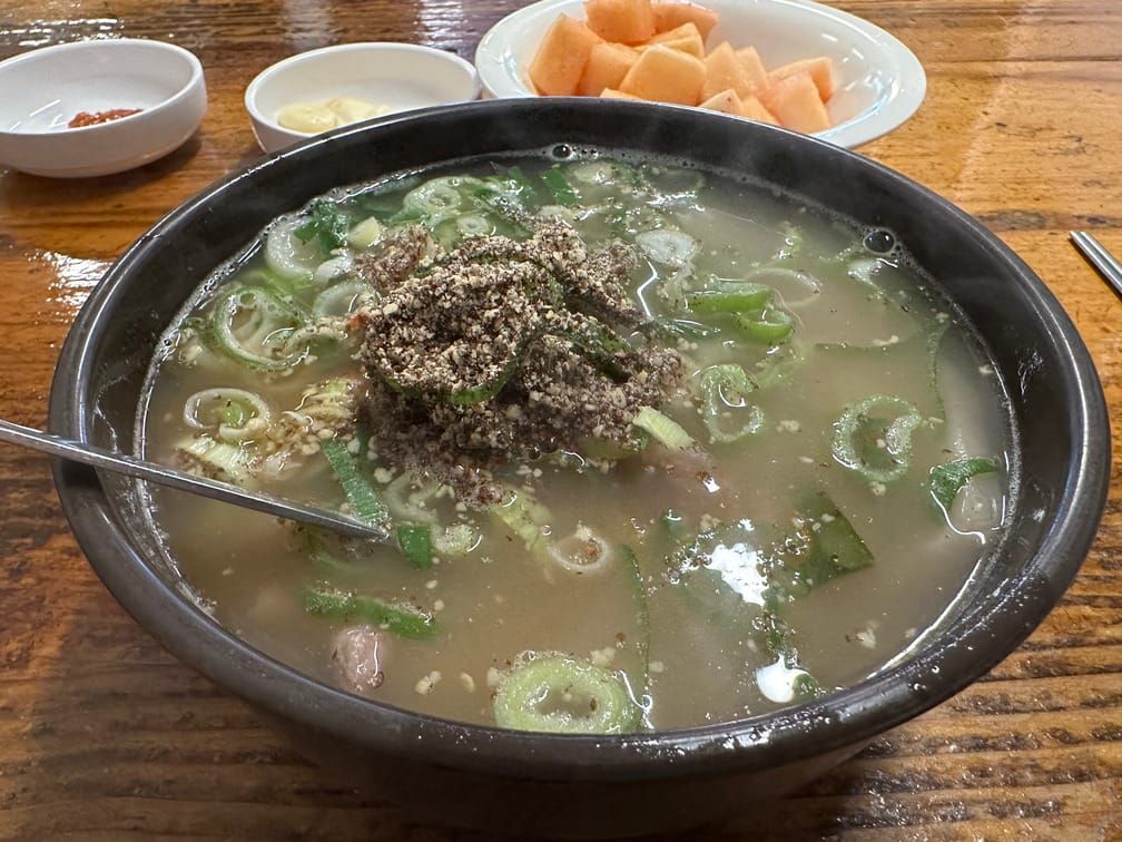 채썬 파와 들깨가루가 올라가고 숟가락이 꽂혀있는, 반쯤 맑은 국물이 담긴 뚝배기.