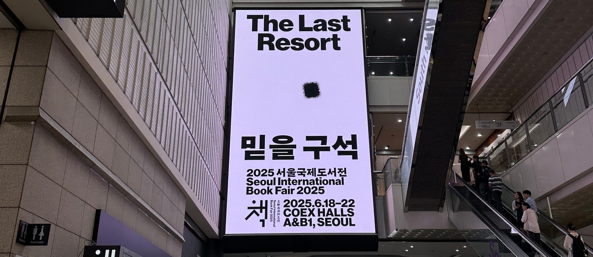 2025 서울국제도서전 알림 전광판. 흰 배경에 검은 글씨로 The Last Resort(믿을 구석)이라는 제목과 도서전의 정보가 표시되어 있다.