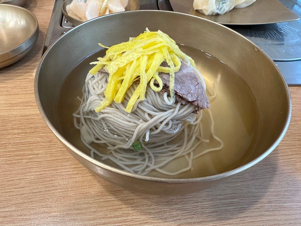 유기그릇에 맑은 국물, 메밀면, 수육, 계란지단으로 구성된 냉면이 차려져 있다.