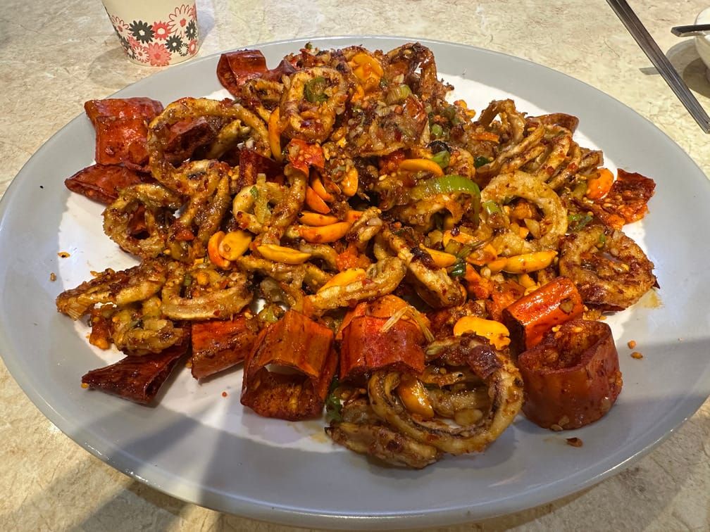 접시 위에 원형으로 잘린 오징어 몸통이 매운 소스로 튀겨져 고추, 땅콩과 함께 버무려져 있다.