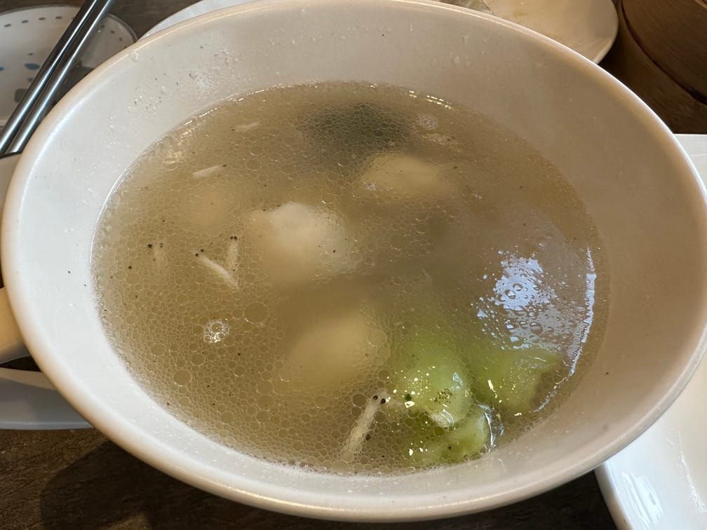 기름이 떠 있는 맑은 국물 아래로 만두와 청경채가 보이는 그릇이 차려진 사진.