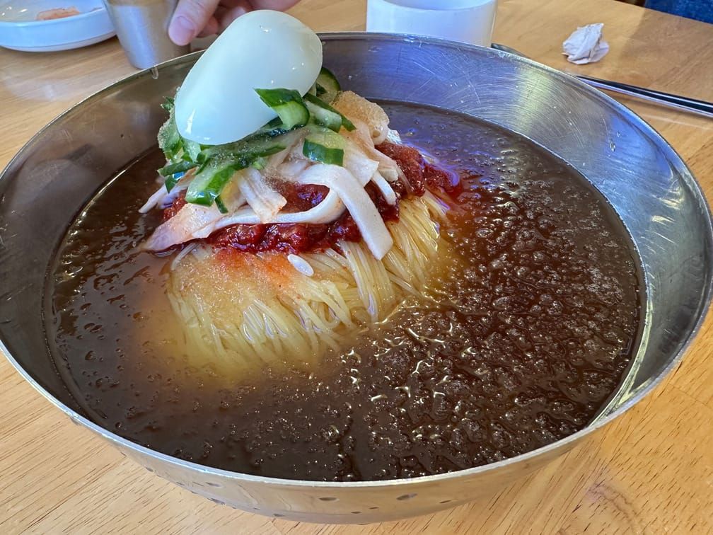 살얼음이 뜬 진한 색 국물에 밀면, 다대기, 무채와 오이채, 달걀 반쪽이 차려진 양은 면기.