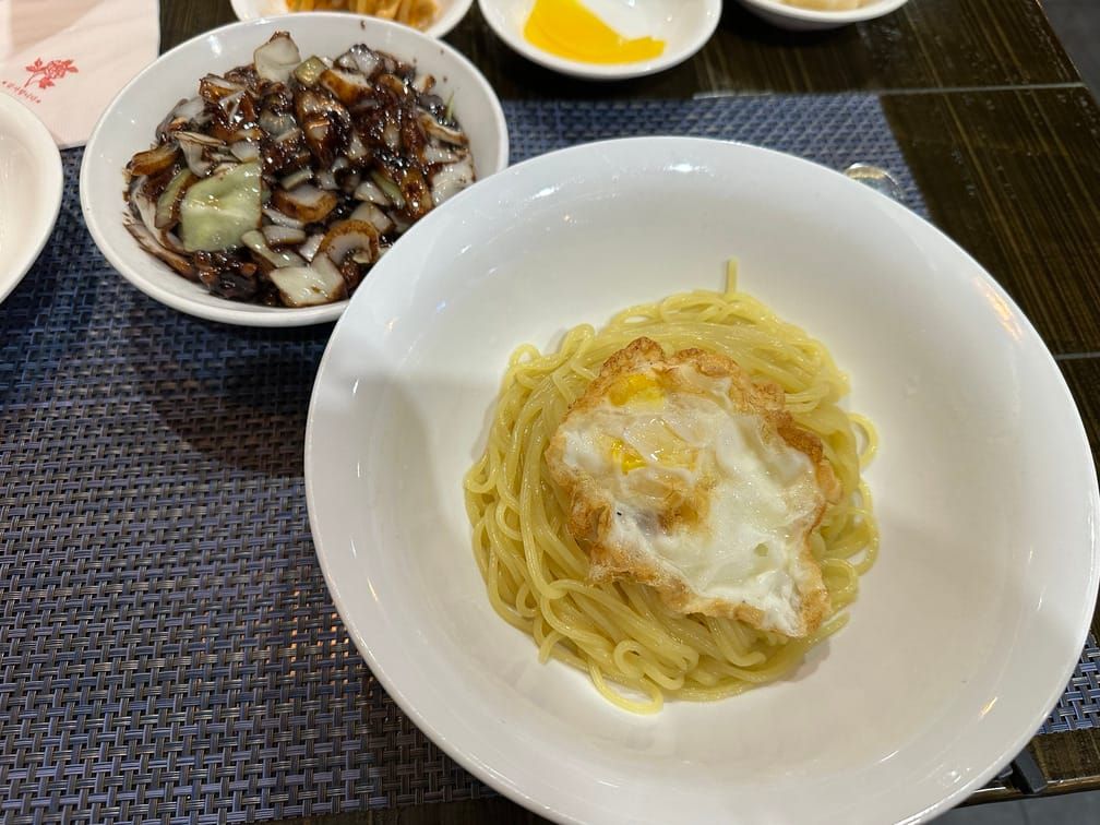 식탁 위에 놓인 중식면과 계란후라이 그릇, 짜장이 담긴 작은 그릇.
