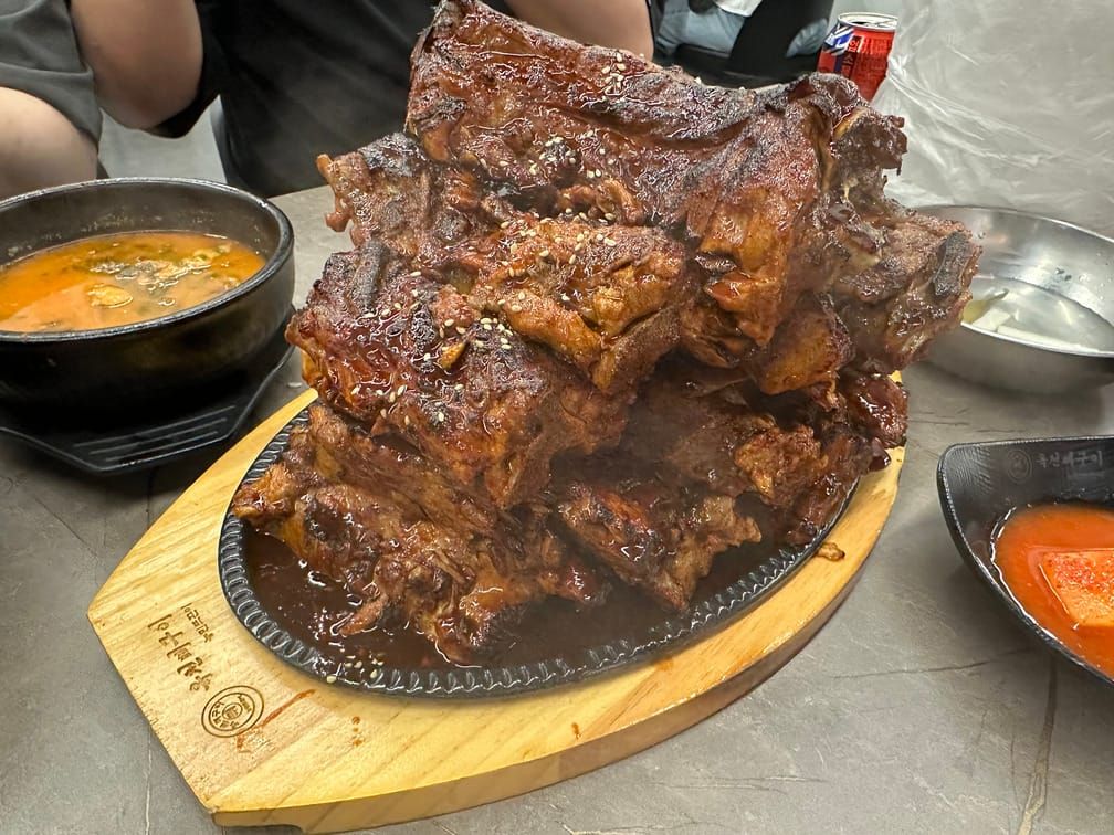 식탁 위 나무받침대 위의 철판 위에 산더미처럼 쌓인, 양념을 발라 구운 등뼈 고기.