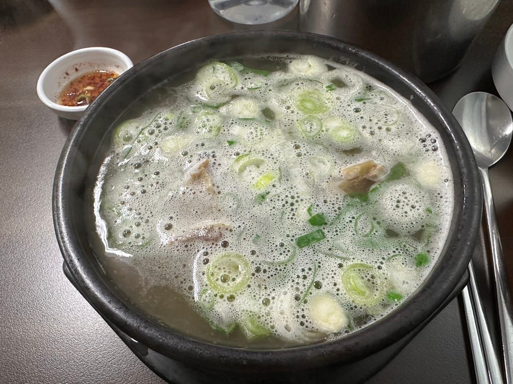 맑은 국물에 파와 거품이 떠 있고 국물 아래 고기가 보이는 뚝배기.