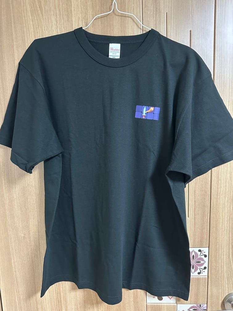 검은 티셔츠의 왼쪽 가슴부분에 가로 네 칸 세로 두 칸의 사각형 격자가 있고, 단검과 돌멩이가 그 안에서 직선으로 연결된 디자인이 들어간 티셔츠.