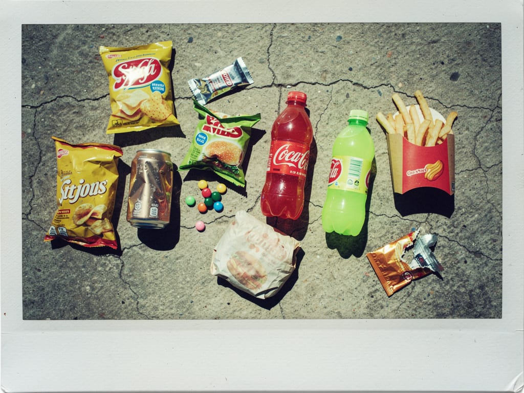 Ultra-processed junk food and sugary drinks on cracked concrete