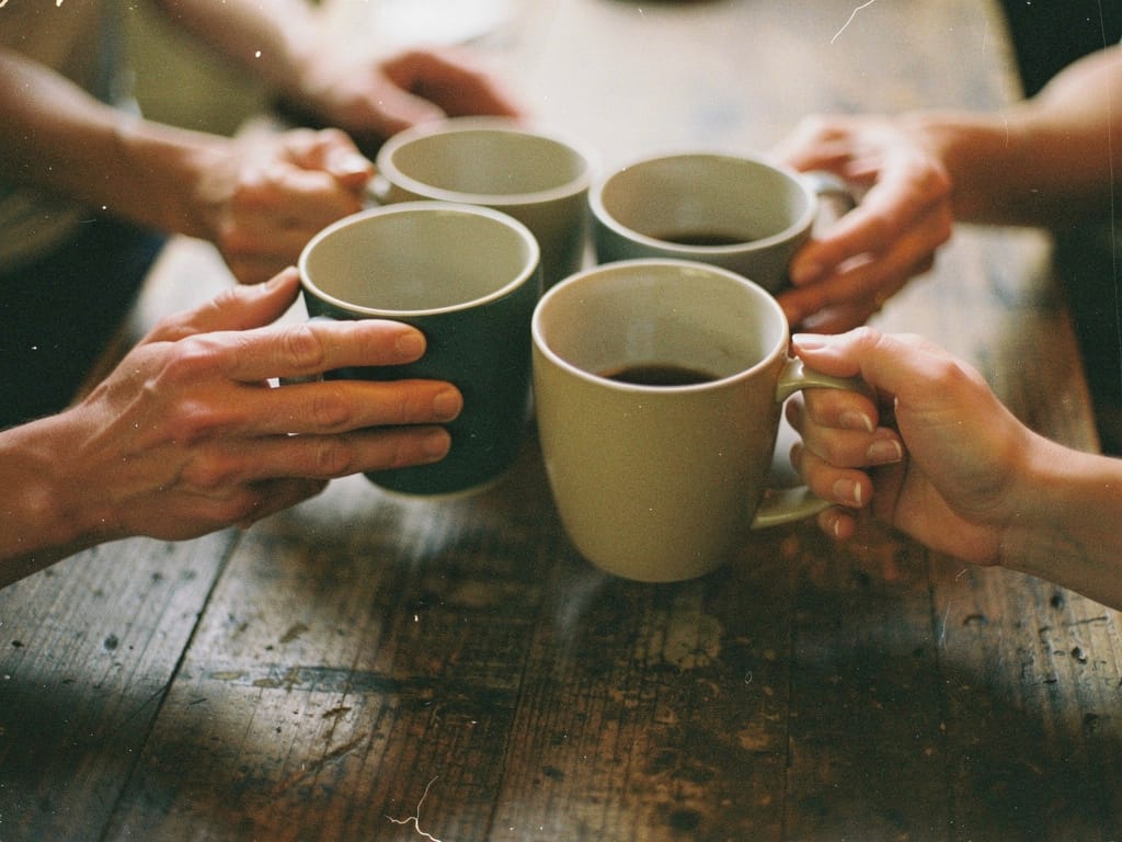 Hands of several people clinking coffee mugs together