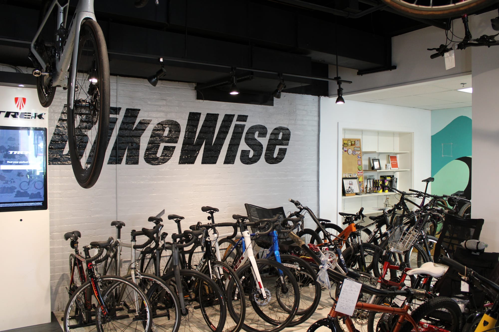 A variety of bikes stand for sale in front of a white brick wall with a "BikeWise" sign