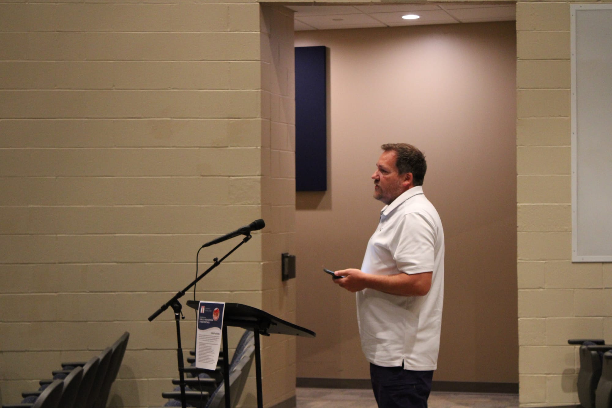 Ivan Carver stands at a microphone, holding his phone
