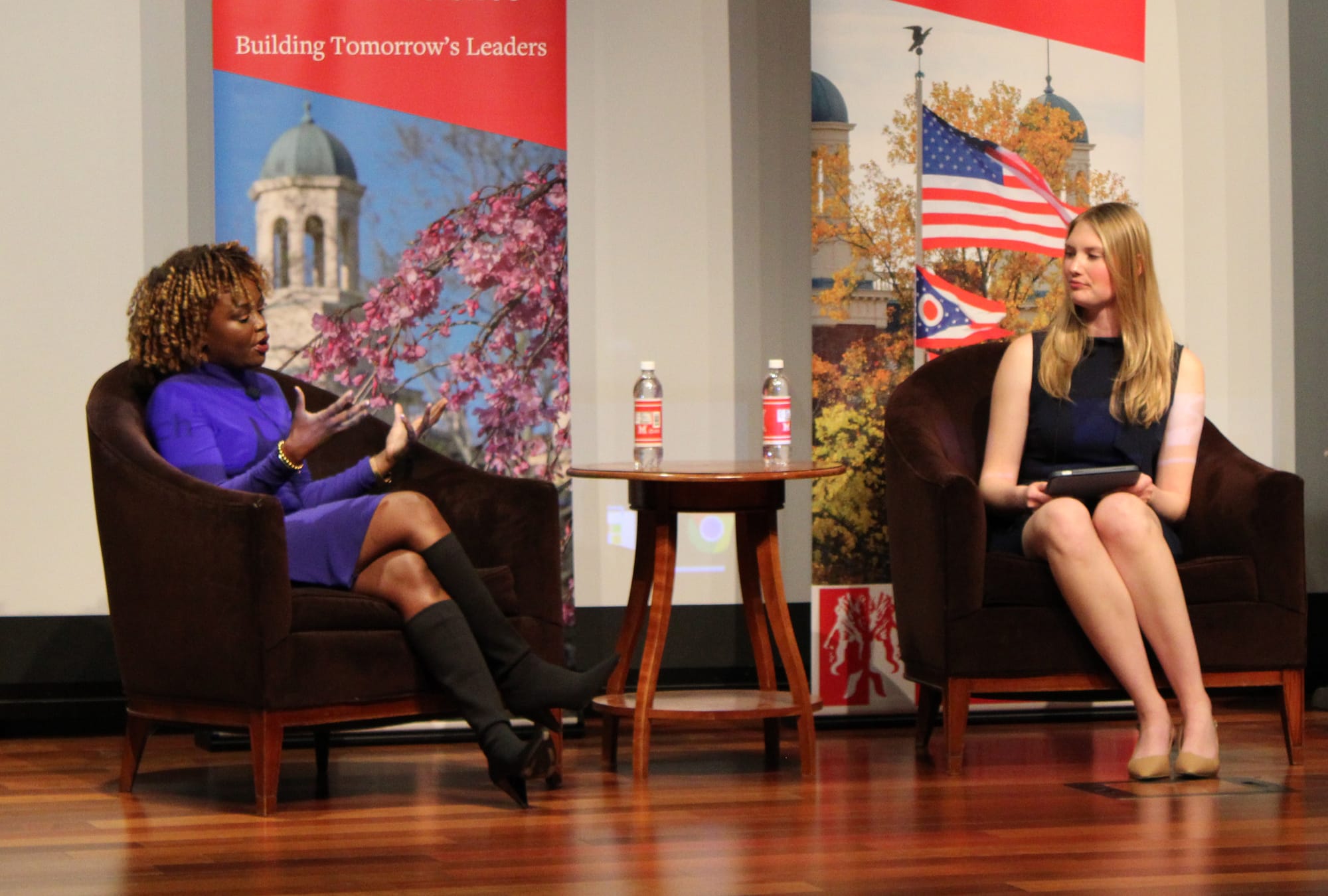 Karine Jean-Pierre and the event moderator sit in chairs on stage