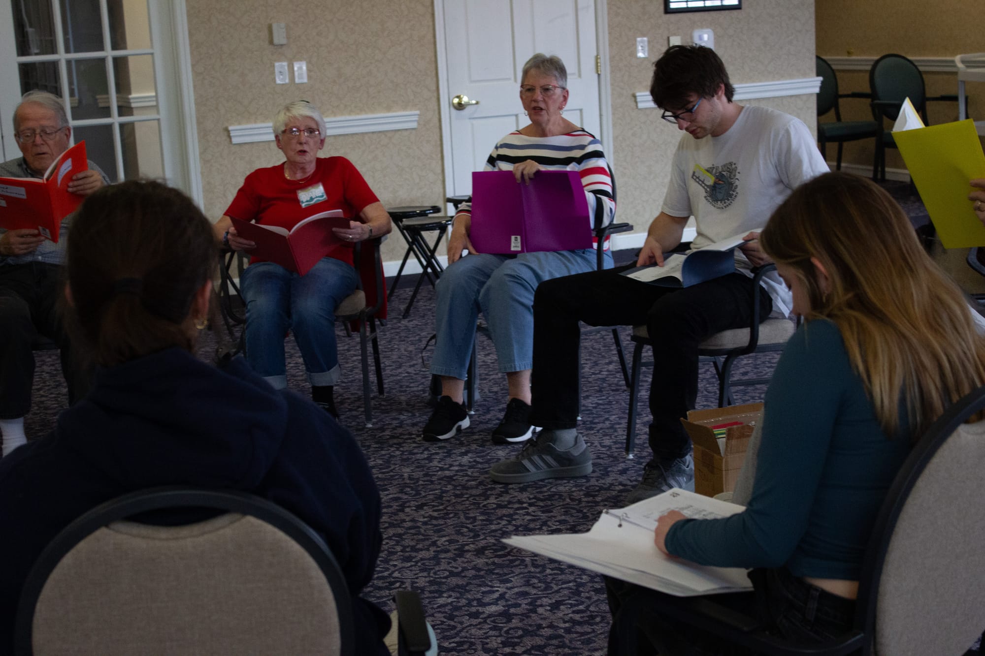 Several choir members sit in a circle and read sheet music
