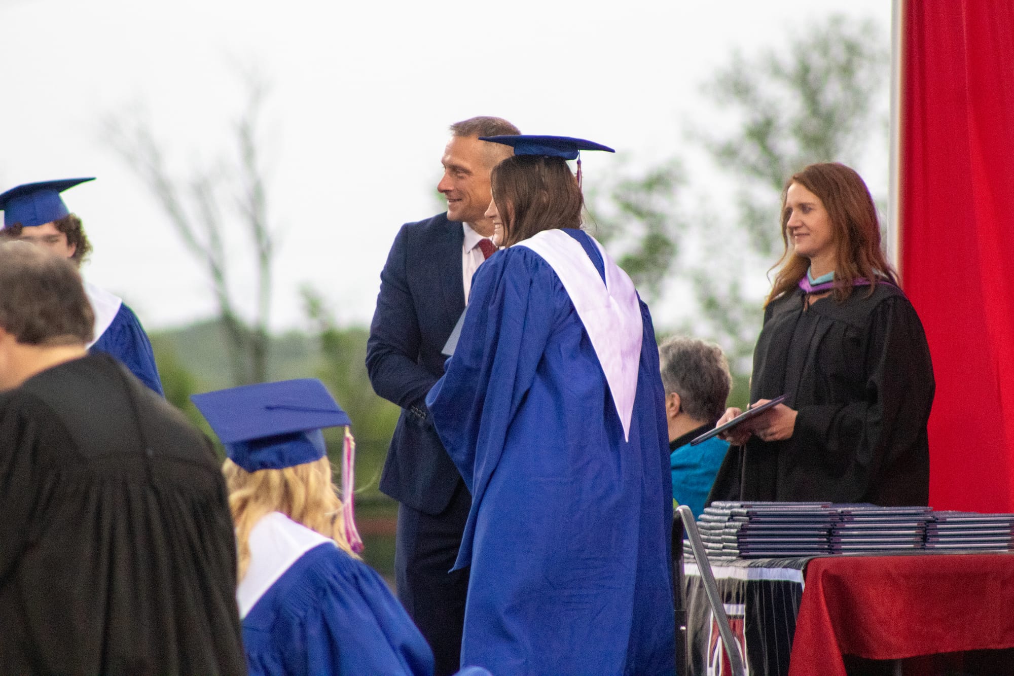 A graduate accepts her diploma onstage and takes a photo with Principal Scott Davie