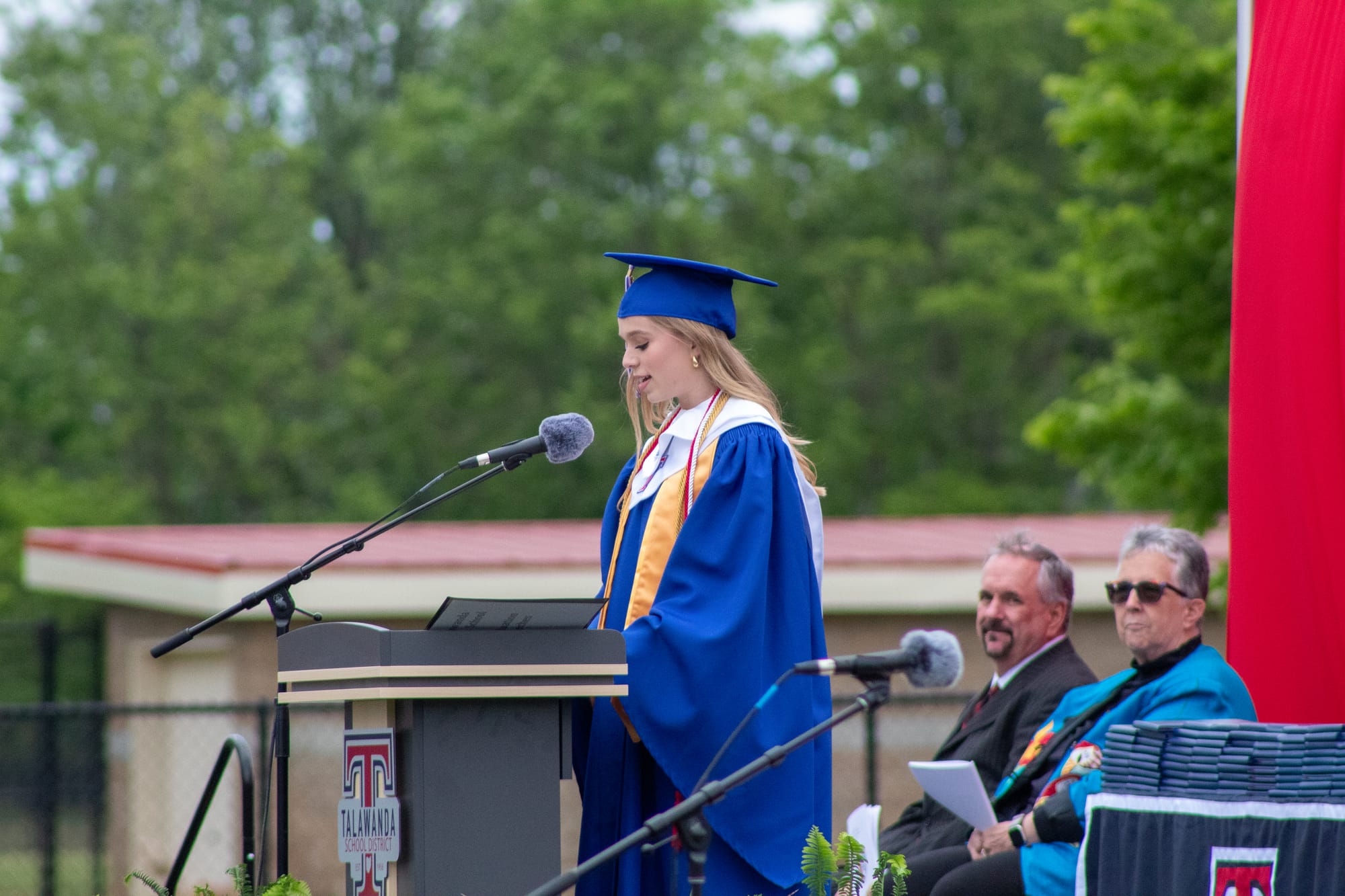 Lilly Chenoweth stands in front of a podium and microphone, giving a speech to her fellow graduates