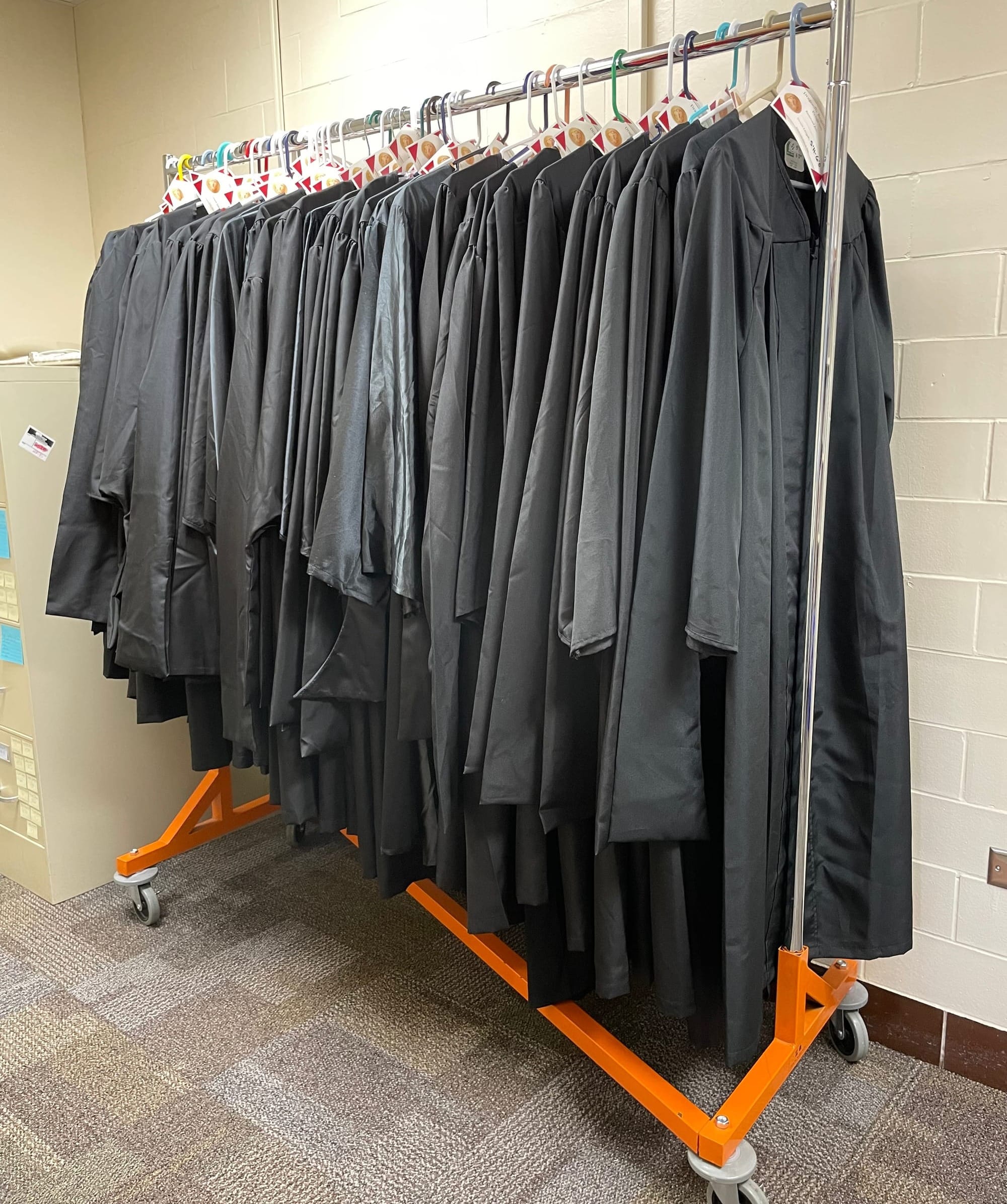 Black graduation gowns hang on a rack, available for borrowing