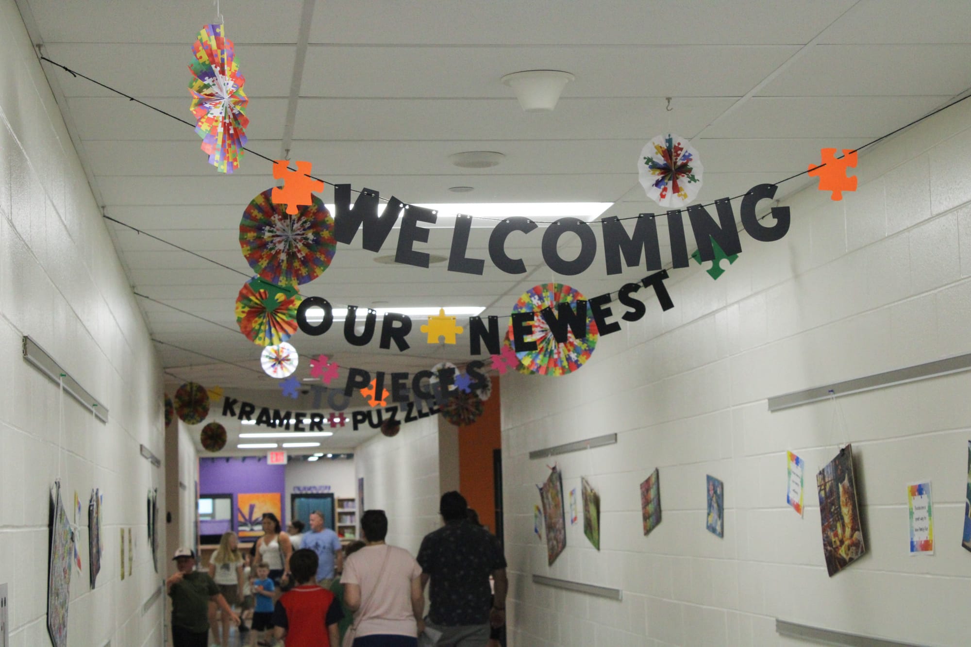 Families walk the halls of Kramer Elementary School. Multiple banners spell out "Welcoming our newest pieces to the Kramer Puzzle."