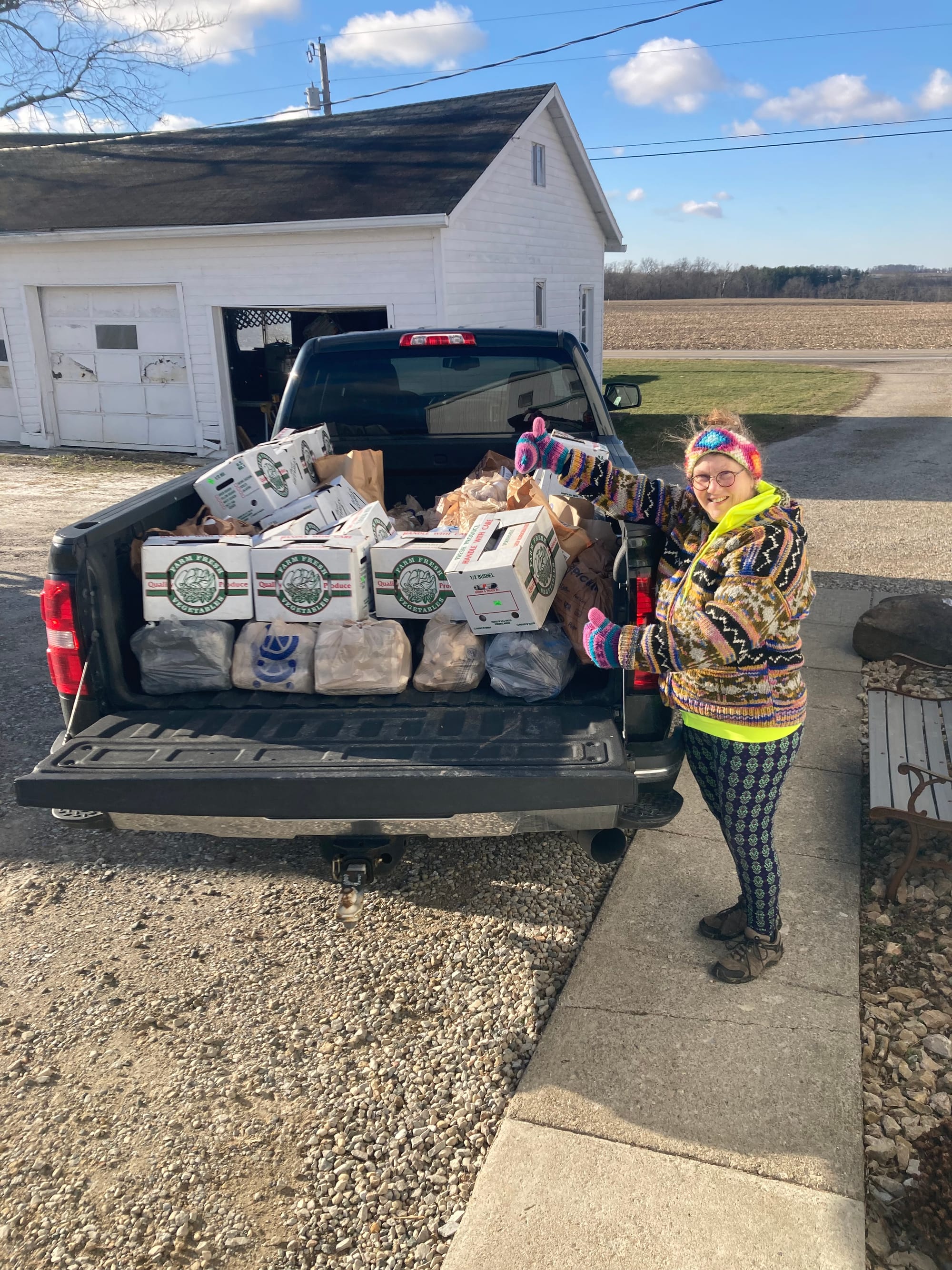 A woman stands next to a truck bed full of plastic bags and boxes.