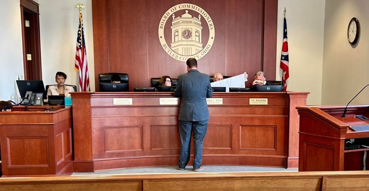 4 Commissioners sit behind their curved wooden desk, adorned with name plaques, and discuss the agenda for the day.