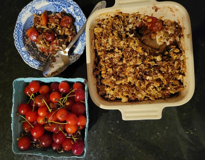 A pint of red cherries in the lower right corner, with pits in a bowl above it. Next to them, a baking dish with cherries and