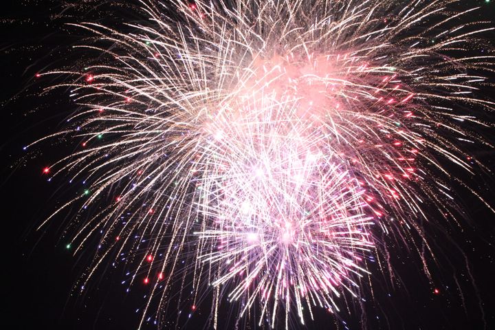 Several red and white fireworks explode in a dark sky at once